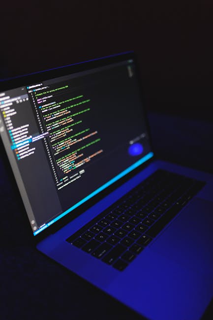 A close-up view of a modern laptop displaying a dark-themed code editor with colorful syntax highlighting, set against a dimly lit background. The laptop's keyboard is visible in the foreground, and t